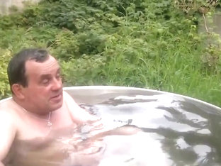 Naked old man rolls around in outside bath tub.